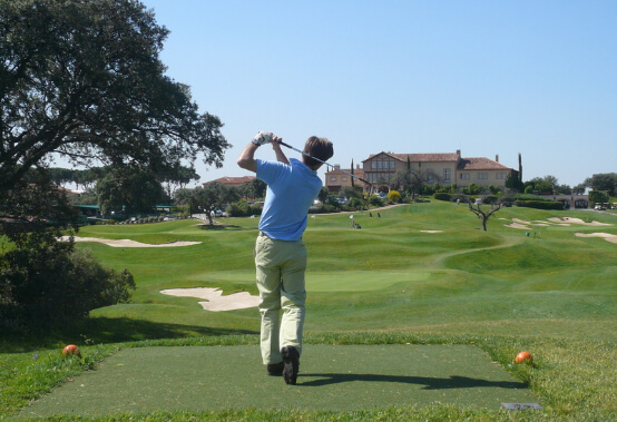 man following through a swing on a course, facing toward the course clubhouse