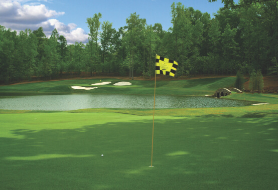 par 3 hole with water feature; hole and flag in foreground with sand traps in background across a pond